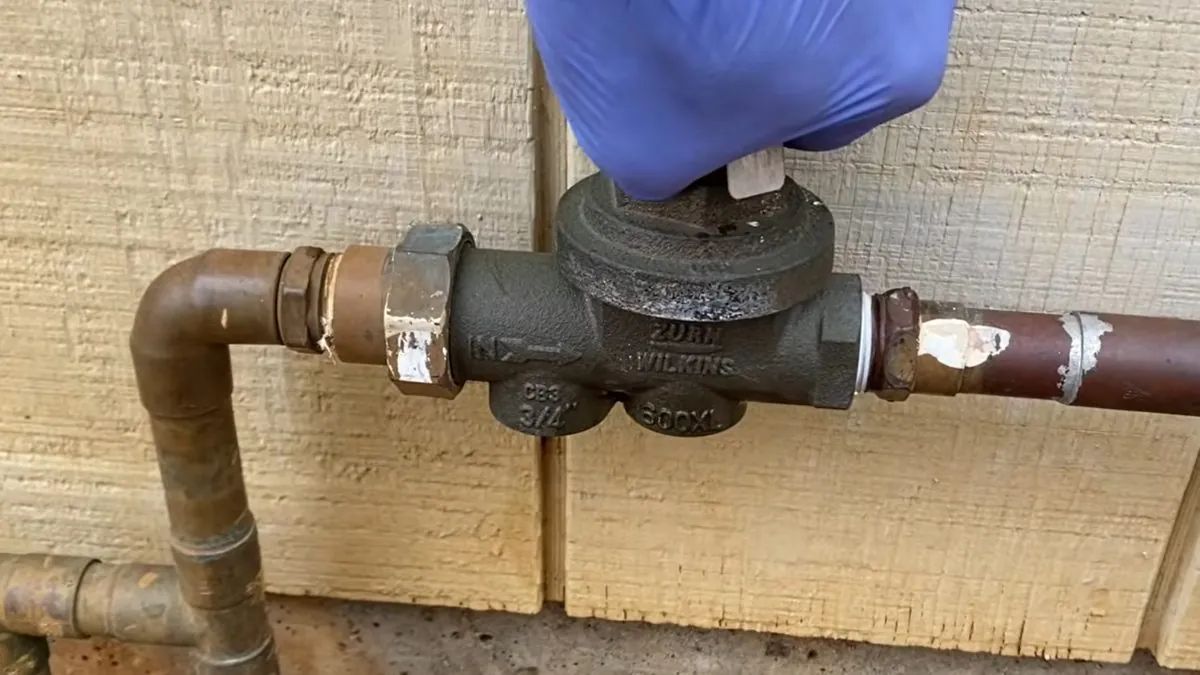 Gloved hand tightening a brass valve on a water line