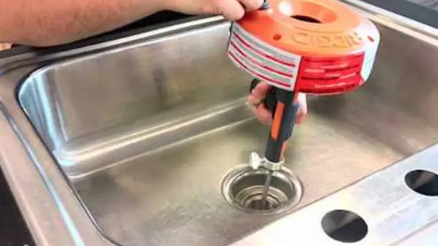 Drain auger held over a stainless steel kitchen sink drain
