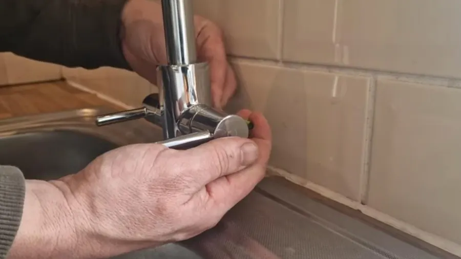 Hands holding the base of a single-handle kitchen faucet against a tile backsplash