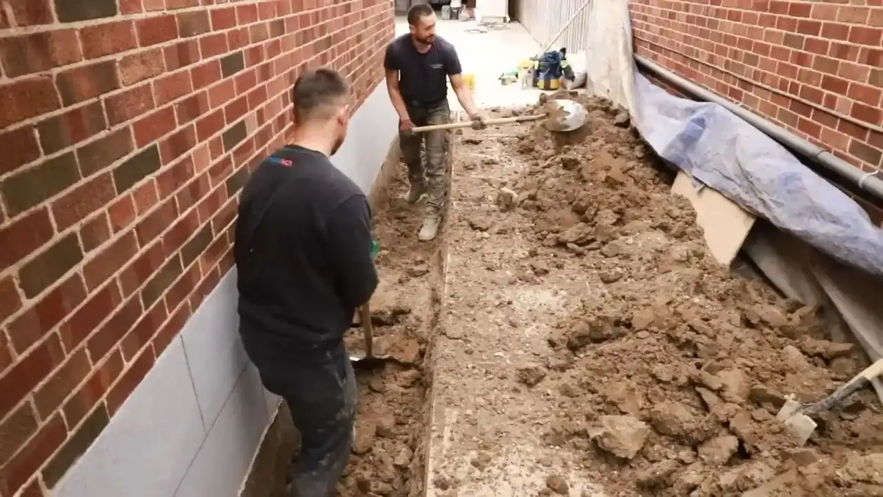 Crew excavating along a brick foundation wall to apply a waterproofing membrane
