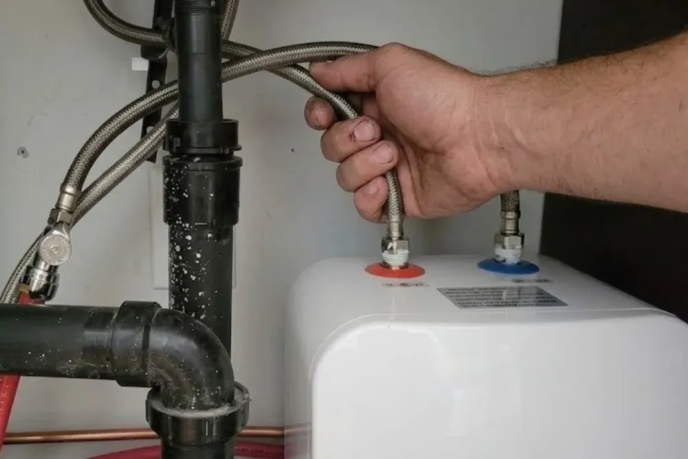 New gas tank water heater set on a drain pan in a garage with copper supply lines